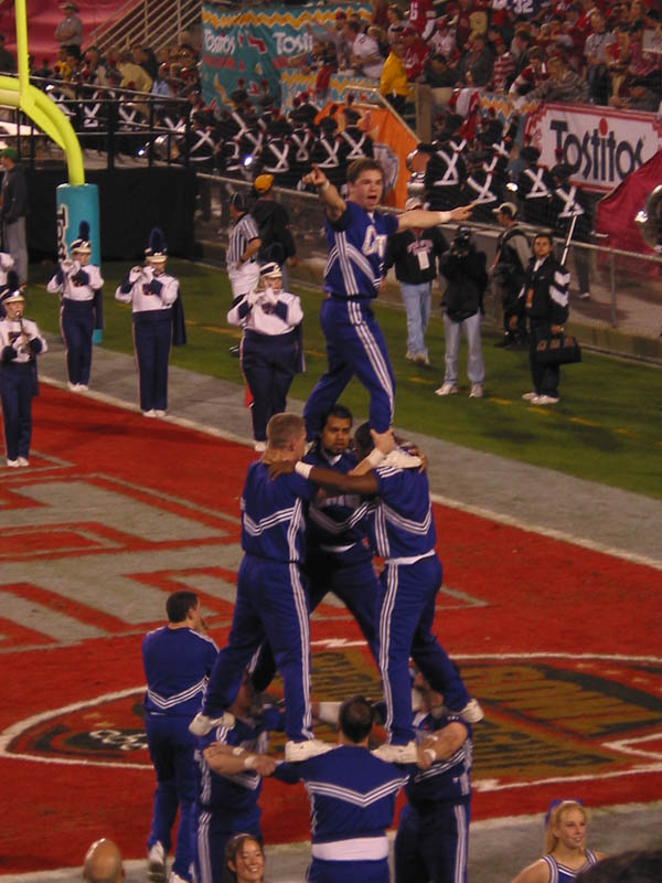 male cheerleaders in a pyramid with band